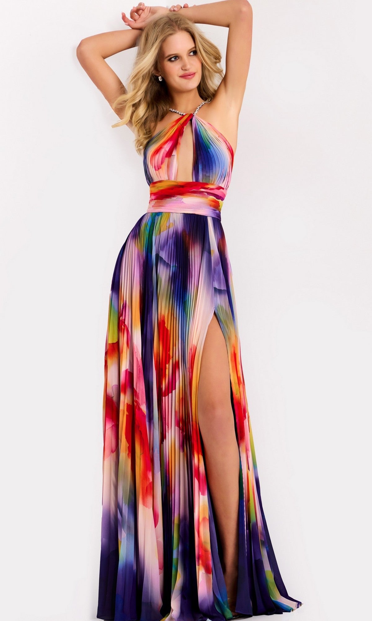 A woman poses in the Jovani 42717 Long Prom Dress, a colorful sleeveless gown with a halter neckline, pleated floor-length skirt, high slit, and flowing silhouette against a plain white background.